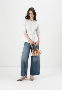Top peplum gris con mangas largas, jeans azul de pierna ancha, zapatos de tacón alto grises y un bolso metálico con un diseño recogido.