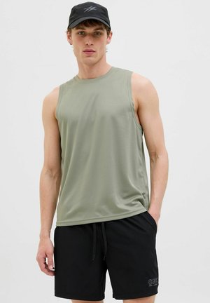 Top sin mangas de color oliva con un acabado texturizado, combinado con pantalones cortos negros que tienen un logo, y llevado con una gorra de béisbol negra.