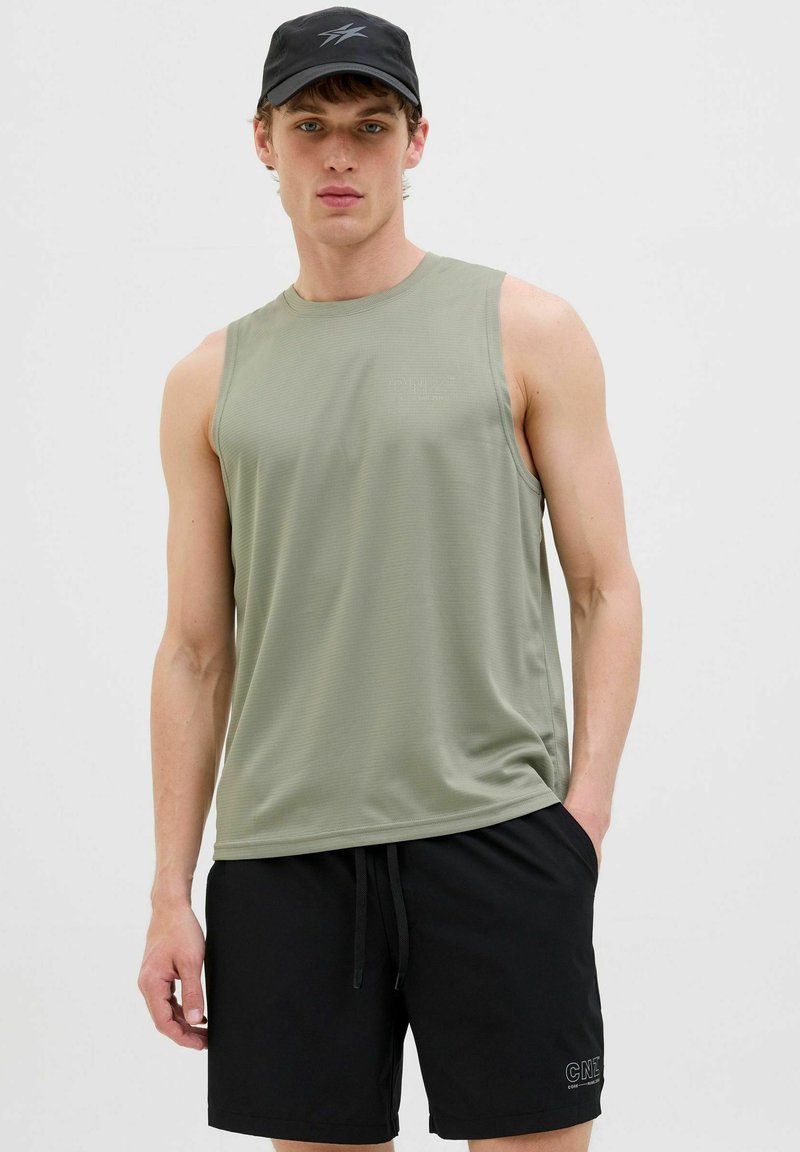 Débardeur olive sans manches avec une finition texturée, associé à un short noir portant un logo, porté avec une casquette de baseball noire.