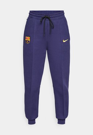 Nike joggebukser i mørk lilla med snøring i livet, sidelommer og en gul logo. Har et brodert FC Barcelona-merke.