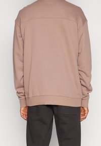 Převlečená mikina v tlumené růžové barvě, vyrobená z texturované bavlněné tkaniny. Má kulatý výstřih, spadená ramena a žebrované manžety.