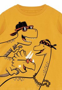 Geel katoenen T-shirt met cartoon-dinosaurussen die zonnebrillen en accessoires dragen. Het ontwerp bevat speelse gezichten en gedurfde lijnen.