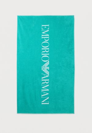 Türkisfarbene rechteckige Handtuch mit weißem, vertikal verlaufendem "EMPORIO ARMANI" Schriftzug und Logo mittig auf dem Handtuch.