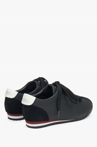 Czarne sneakersy z mixem gładkiego i zamszowego materiału, okrągłym czubkiem oraz białym akcentem na pięcie z czerwoną i białą paskowaną podeszwą.