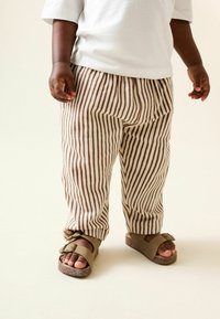 Gestreifte Leinenhose in Braun und Creme, mit entspanntem Schnitt und Kordelzugbund, kombiniert mit braunen Sandalen mit doppelten Schnallen.