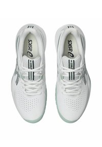 Des chaussures de tennis blanches avec un dessus perforé, des accents verts et un logo sombre. Les lacets et une semelle rembourrée sont visibles de la vue de dessus.