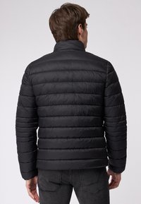 Giacca nera imbottita con motivo a righe orizzontali, colletto alto e design elegante. Il materiale appare sintetico e liscio.