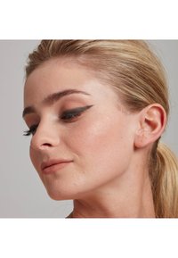 Primo piano di un volto con tono di pelle beige, capelli biondo chiaro raccolti, eyeliner a guida affilata, un leggero fard e labbra dal aspetto naturale.
