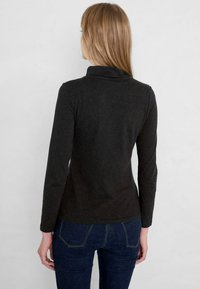 Mörkgrå långärmad topp med hög krage, slim fit och mjuk textur, tillsammans med mörkblå jeans med bakfickor.