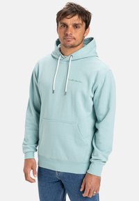 Light blue hoodie made of cotton, featuring a front kangaroo pocket, white drawstrings, and a small logo on the chest. Casual fit.