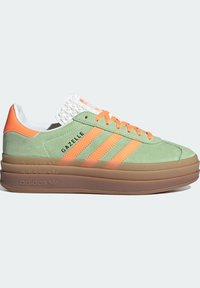 Sneaker in camoscio verde chiaro con accenti arancioni, tre strisce, linguetta bianca texturizzata e suola spessa in gomma. Branding "Gazelle" sul lato.