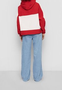 Czerwona i biała kurtka z kapturem o oversize'owym kroju, z kolorowym blokiem i elastycznymi mankietami, noszona na jasnoniebieskich szerokich spodniach.