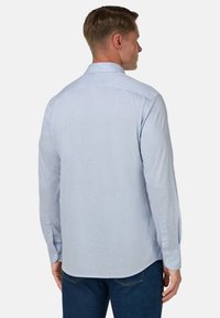 Himmelblaues Langarmhemd aus weichem Stoff mit klassischem Kragen und geknöpften Manschetten, mit abgerundetem Saum und subtiler Textur.