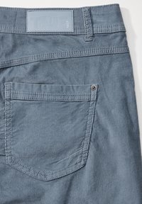 Grå kordfløyelsmateriale med en jevn tekstur. Har en baklomme med en metallrivet og en merketapp på midjebåndet.