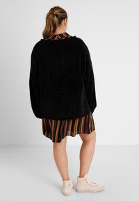 Black, textured oversized sweater layered over a multicolored striped shirt dress, paired with light beige high-top sneakers.