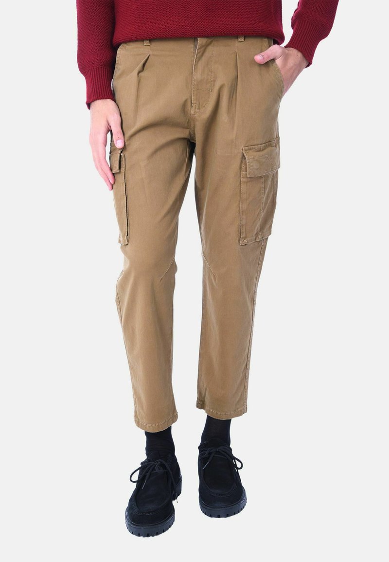 Pantaloni cargo khaki con una vestibilità rilassata, due tasche laterali e design plissettato. Abbinati a scarpe e calze nere; materiale in cotone.