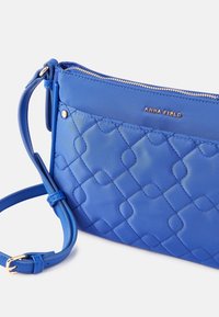 Borsa a tracolla blu trapuntata con finitura liscia, dotata di una cerniera e dettagli del logo in tonalità oro. Include una tracolla regolabile.