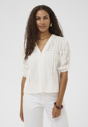 Biela blúzka so zapínaním na gombíky a nafúknutými rukávmi, zdobená výšivkou s otvormi a výstrihom do V. Vyrobená z ľahkej látky.