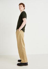 Dark green fitted t-shirt paired with beige wide-leg pants and black leather shoes with yellow stitching. Minimalist design and classic colors.
