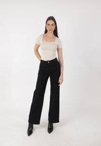 Top beige aderente con scollo quadrato, pantaloni neri a gamba larga a vita alta con striature metalliche verticali, abbinati a stivaletti neri a punta.