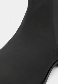 Botín negro hasta el tobillo con un acabado suave y mate y una silueta elegante. Presenta una punta redondeada y detalles de costura mínimos.