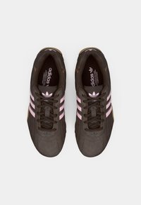 Hnedé športové topánky s ružovými pruhmi, textúrovaný zvršok, ploché šnúrky a gumové podrážky. Obsahujú logo Adidas na jazyku a strane.