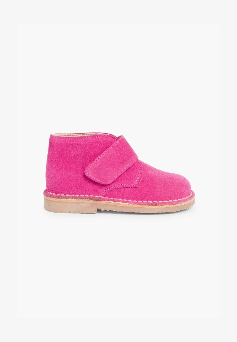 Cizmă până la glezna din suede roz cu o curea cu arici, talpă din cauciuc bej și detalii de cusătură în jurul bazei. Design clasic pentru o purtare ușoară.