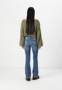 Överdimensionerad grön stickad tröja med vida ärmar, kombinerad med figurnära blå utsvängda jeans. Diskret textur och en avslappnad passform är framträdande egenskaper.