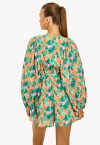 Mono floral verde con mangas abullonadas, que presenta patrones en rosa y naranja de flores y hojas. Diseño con cintura elástica y ajuste relajado.