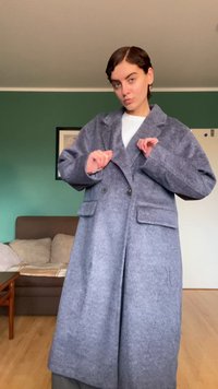 Cappotto in misto lana grigio con design doppiopetto, ampi revers e due tasche frontali. Tessuto strutturato, lunghezza al ginocchio con vestibilità morbida.