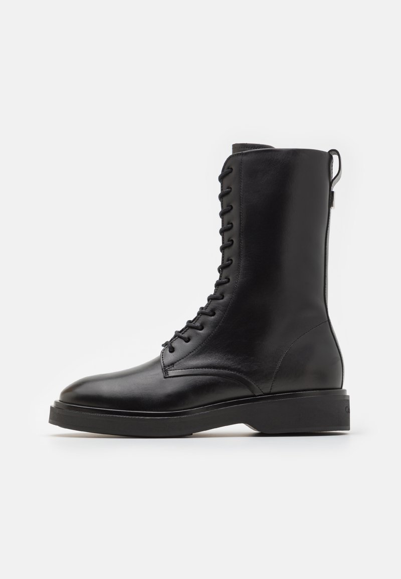 Bottine en cuir noir avec une texture lisse, lacets à l'avant et semelle épaisse noire. Dispose d'une languette au dos pour un enfilage facile.