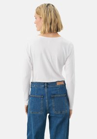 Long-sleeve white top paired with blue high-waisted jeans. The jeans feature standard back pockets and a leather label at the waistband.