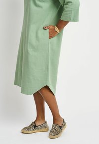 Green linen dress with three-quarter sleeves and side pockets, paired with animal print espadrilles featuring a jute sole and black accents.