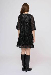 Vestido negro, holgado, con un diseño texturizado de punto abierto y mangas cortas, combinado con botas negras brillantes hasta la rodilla.
