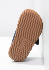 Rubberen schoenzool met een gestreept patroon, in een tan kleur en met geïmporteerde branding. De vorm is plat met ronde randen.