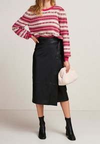 Pull à motifs rouge et blanc avec des manches longues, associé à une jupe en cuir noir à enrouler. Accessoirisé avec un sac à main texturé beige clair.