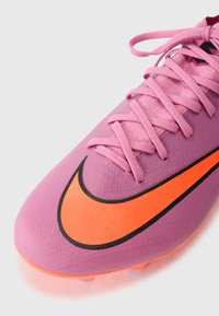 Pink soccer cleat with textured surface, black outline, and prominent orange Nike swoosh. Features pink laces and molded studs for traction.