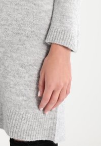 Maglione lavorato a maglia grigio chiaro con orlo e polsini a costine, dal tocco morbido. Presenta un dettaglio con spacco laterale per un tocco di stile in più.