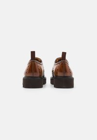 Brown leather shoes with a rounded toe, decorative perforations, and a brown sole. Elastic pull tab at the heel for easy wear.