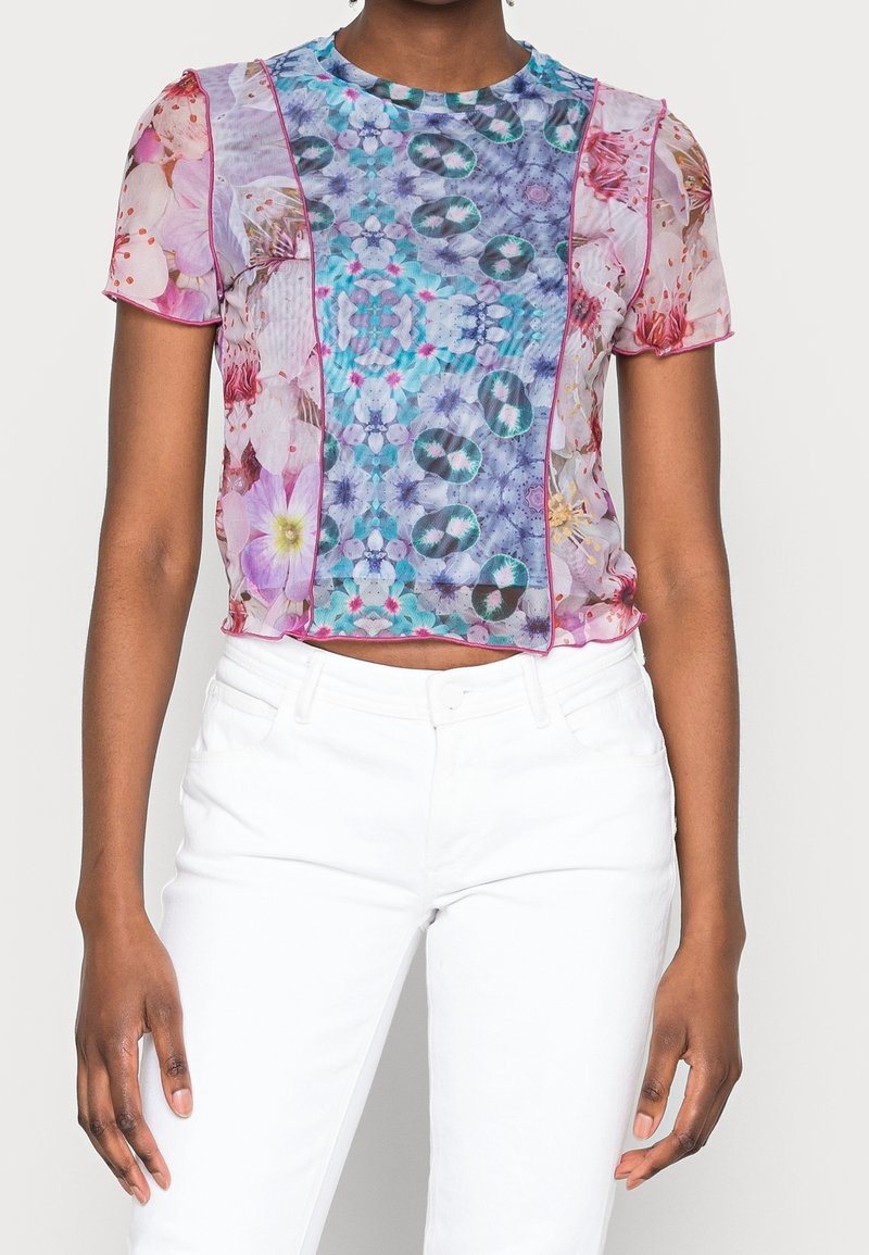 Top corto de manga corta transparente con un patrón floral y geométrico en púrpura, rosa y azul, con costuras en rosa contrastantes. Diseño recortado.