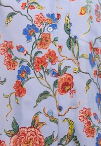 Tissu à motif floral bleu clair, avec des motifs floraux rouges, bleus et verts, agrémenté de petits boutons bleus et d'une texture douce.
