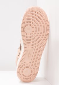 Nike-sneakersula i ljusrosa med cirkulära och vågmönster, med texturerade kanter och ett jämnt centralt område.