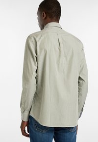 Camisa de manga larga a rayas verdes y blancas con cuello clásico, pliegue en la espalda y puños abotonados, combinada con vaqueros de mezclilla azul.