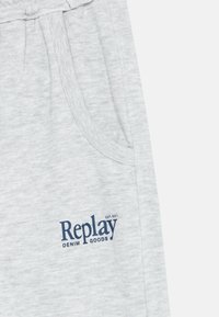 Ljust grå sweatpants med sidfickor, prydda med en blå "Replay Denim Goods"-logotyp. Tillverkade av ett mjukt, texturerat tyg.
