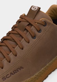 Καφέ δερμάτινο αθλητικό παπούτσι με κορδόνια στο ίδιο χρώμα, μαύρες τρύπες για τα κορδόνια, λαστιχένια σόλα και λογότυπο SCARPA στο πλάι.