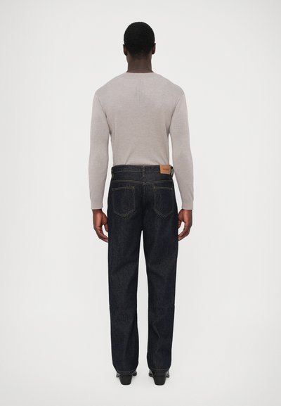 Tamno prani traperice s ravnim krojem, s leđnim džepovima i kožnom oznakom na pojasu. U kombinaciji sa svijetlosivim rebrastim puloverom.