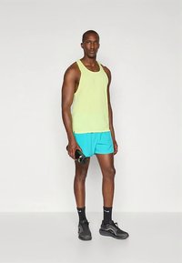 Vyriška sportinė apranga, kurioje ryškiai geltona marškinėlių be rankovių ir turkio spalvos šortai. Modelis laiko juodą vandens butelį ir dėvi juodus sportinius batelius.