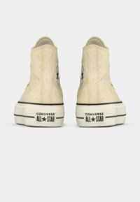 Ψηλές αθλητικές μπότες σε ανοιχτό κίτρινο υφασμάτινο καμβά με μαύρο λογότυπο αστέρι, λευκή καουτσούκ σόλα και αντίθετους μαύρους ρίγες στη βάση.