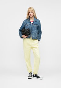 Denim jaka ar pogām, gaiši zils; dzelteni sporta bikses, elastīgi rokturi; melna rokassoma; melnas kedas ar baltām akcentēm.