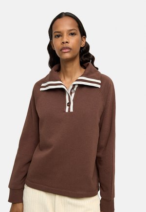 Brązowy sweter z kołnierzem w białe paski, zapinany na dwa guziki, z długimi rękawami, wykonany z teksturowanej tkaniny. Stylizowany z jasnymi spodniami.